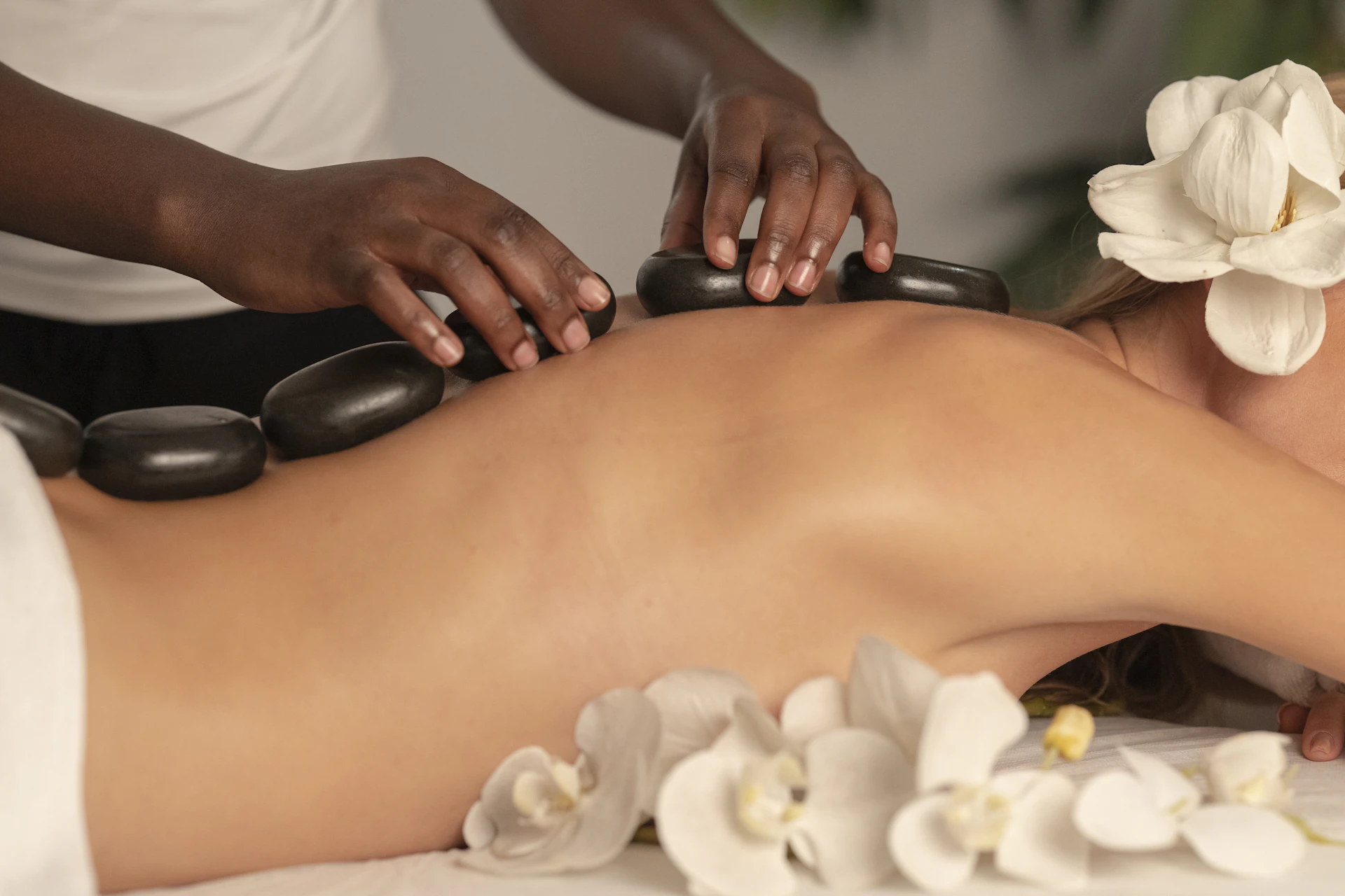 Hot-Stone-Massage mit warmen Basaltsteinen und Frangipani-Blüten